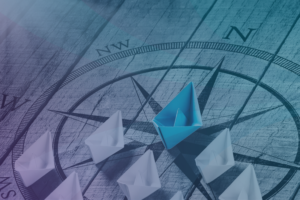 Leadership Image Showing A Compass With White Paper Boats Following A Blue Paper Boat
